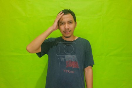 Asian man has a headache isolated on green background