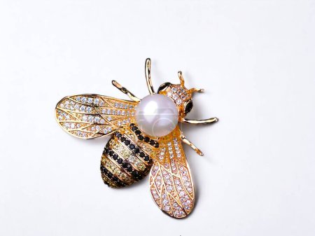 Gold jewelery in the shape of a bee on a white background