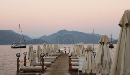 Foto de Mugla, Marmaris Turquía - 31 de julio de 2020: Muelle con sombrillas cerradas y barcos a la hora dorada en un día de verano. Enfoque selectivo - Imagen libre de derechos