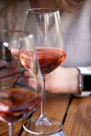 Foto de Vino rosa. Foto vertical de dos copas de vino rosa sobre una mesa de madera con una mujer - Imagen libre de derechos