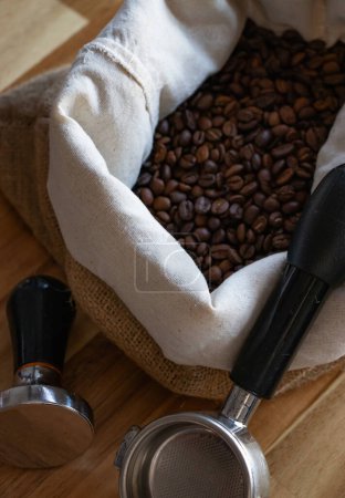 Foto de Foto vertical de granos de café en la bolsa. Granos de café en la bolsa y herramientas de café negro en la mesa de madera. Enfoque selectivo. - Imagen libre de derechos