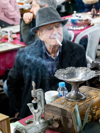 Foto de Un anciano fumando en su puesto vintage en el bazar. Este bazar conocido como en turco "Ayranci Antika Pazari" - Imagen libre de derechos