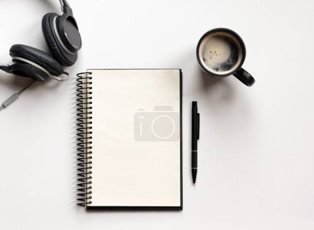 Foto de Moderna mesa de escritorio de oficina blanca con portátil, bolígrafo, auriculares y taza de café. Página de cuaderno en blanco para la entrada de texto en el medio. Vista superior, plano. - Imagen libre de derechos