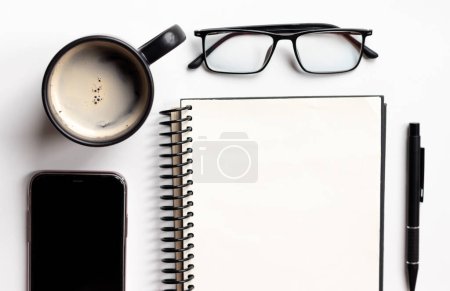 Foto de Mesa de escritorio de oficina con una taza de café, portátil, lápiz, vasos y teléfono inteligente aislado sobre fondo blanco. Vista superior con espacio de copia, plano. - Imagen libre de derechos