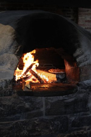 Steinpizzaofen mit loderndem Feuer und Pizzakochen im Inneren