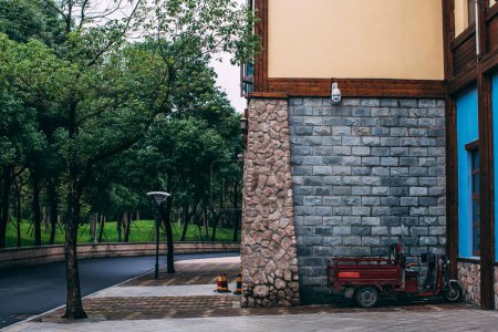 Ziegelsteinmauer eines Gebäudes im chinesischen Park. Asphaltstraße, Motorrad, Bäume. China, Provinz Anhui