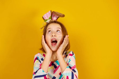 Photo for Happy playful teenager girl wearing bunny ears on a bright yellow studio background, celebrating Easter in style. - Royalty Free Image