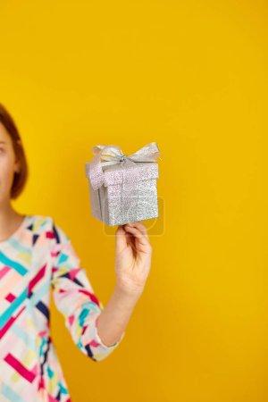 Photo for Hand of child teenage girl hold silver present box on a yellow background, kid hold gift box, birthday, holiday concept - Royalty Free Image
