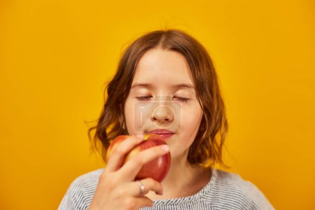 Foto de Linda chica adolescente, niño come, muerde una manzana roja fresca aislada en el fondo amarillo del estudio, opciones de bocadillos saludables, concepto de estilo de vida de alimentos saludables, espacio para copiar - Imagen libre de derechos