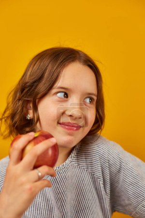Foto de Linda chica adolescente, niño come, muerde una manzana roja fresca aislada en el fondo amarillo del estudio, opciones de bocadillos saludables, concepto de estilo de vida de alimentos saludables, espacio para copiar - Imagen libre de derechos