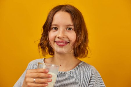 Foto de Linda chica adolescente, niño con un vaso de leche fresca aislada en el estudio de fondo amarillo, huesos fuertes, leche para el crecimiento, concepto de estilo de vida saludable, espacio de copia - Imagen libre de derechos