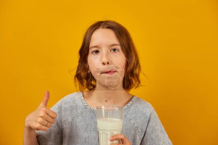 Foto de Linda chica adolescente, niño con un vaso de leche fresca aislada en el estudio de fondo amarillo, huesos fuertes, leche para el crecimiento, concepto de estilo de vida saludable, espacio de copia - Imagen libre de derechos