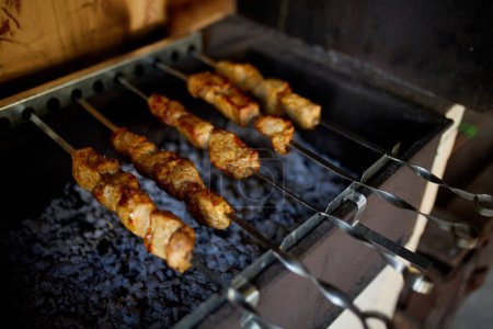 Foto de Agitadores de kebabs cocinan sobre las brasas calientes de una parrilla de barbacoa en un entorno de patio trasero casero, destacando una tradición culinaria de verano. - Imagen libre de derechos
