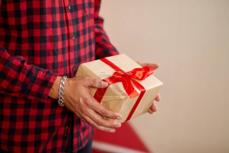 Photo for Close-up of hands holding a gift box with a red ribbon against a red background. - Royalty Free Image