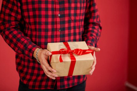 Foto de Primer plano de las manos sosteniendo una caja de regalo con una cinta roja sobre un fondo rojo. - Imagen libre de derechos