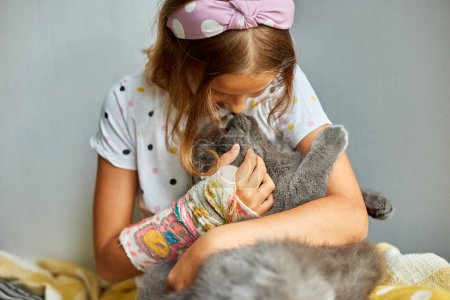 Teen girl with a broken arm orthopedic cast play with cat at home, love pets.