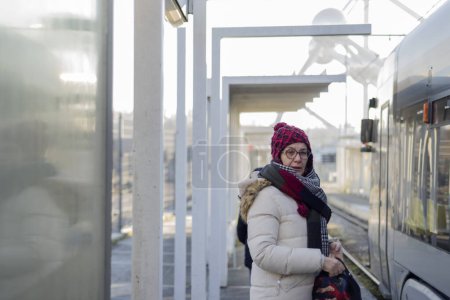 Femme adulte avec bonnet en laine, attend à la station de tram à Bruxelles pour aller travailler. En arrière-plan l'atome