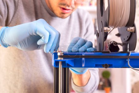 Foto de Primer plano de la mano de un hombre con guantes azules calibrando una impresora 3D. - Imagen libre de derechos