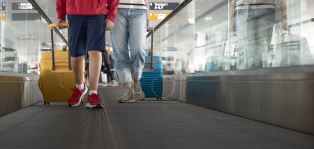 Zwei Personen, ein Kind und ein Erwachsener, mit Gepäck auf einem Laufsteg am Flughafen.