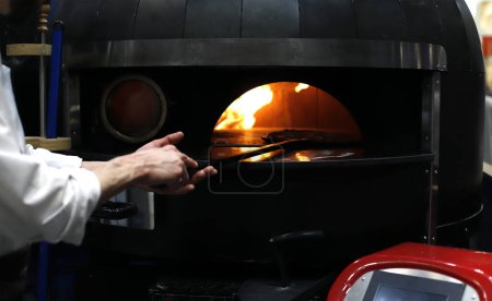 Photo for Professional chef taking a pizza out of the oven - Royalty Free Image