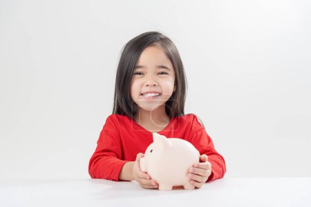 Téléchargez les photos : Petite fille asiatique économiser de l'argent dans une tirelire, apprendre à épargner, Enfant économiser de l'argent pour l'éducation future. Concept d'argent, de finances, d'assurance et de personnes - en image libre de droit