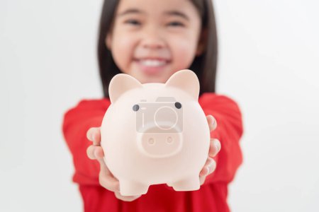 Téléchargez les photos : Petite fille asiatique économiser de l'argent dans une tirelire, apprendre à épargner, Enfant économiser de l'argent pour l'éducation future. Concept d'argent, de finances, d'assurance et de personnes - en image libre de droit