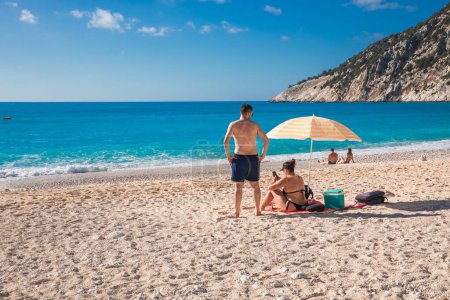 Foto de Una joven pareja descansa en la playa de Myrtos, isla de Cefalonia, Grecia, durante las vacaciones de verano en el mar. Horizontal. - Imagen libre de derechos