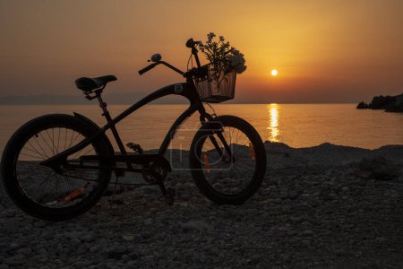 A bicycle with flowers against the background of a spectacular sunset on a hot summer evening in Greece. Horizontal.