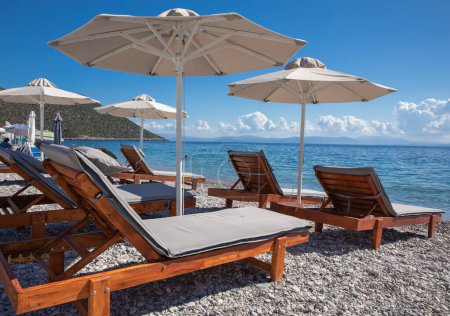 White umbrellas, sunbeds on sandy pebble beach with turquoise crystal clear water in Tyros town, Peloponnese, Argolic Gulf, Myrtoan Sea, GREECE in summer morning. Horizontal.