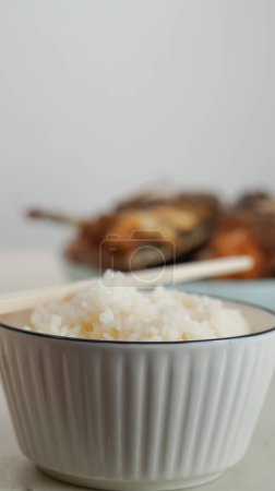 Weißer Reis in einer Schüssel und gebratener Fisch auf einem weißen Teller werden auf dem Tisch serviert