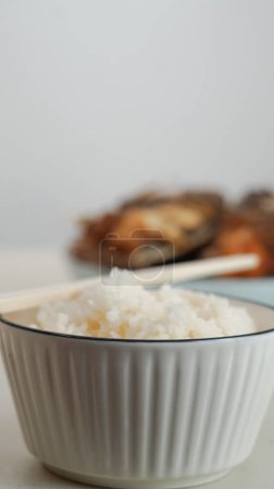 Weißer Reis in einer Schüssel und gebratener Fisch auf einem weißen Teller werden auf dem Tisch serviert