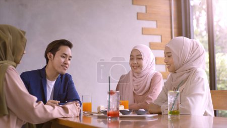 Photo for A group of successful upwardly mobile Asian Muslim friends relish a tranquil coffee shop gathering on a bright and joyful sunny day - Royalty Free Image