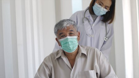 Téléchargez les photos : Une femme asiatique médecin poussant un homme adulte âgé souffrant de maux de dos d'une hernie du disque rachidien dans son fauteuil roulant se déplaçant dans le couloir de l'hôpital - en image libre de droit