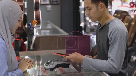 Foto de Un musulmán asiático ascendentemente móvil que usa un teléfono móvil: smartwatch para pagar un producto en una terminal de venta con pago de identificación nfc para verificación y autenticación - Imagen libre de derechos