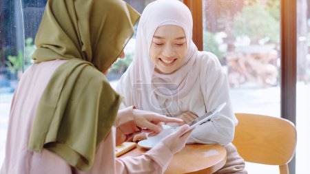 Foto de Jóvenes hermosas mujeres musulmanas asiáticas disfrutando de un momento relajante trabajando y jugando con el teléfono móvil en la cafetería en un día soleado brillante - Imagen libre de derechos