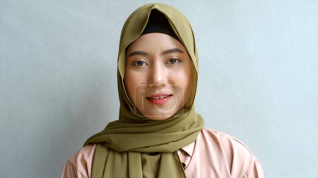 Photo for Close Up Portrait of a Young Asian Muslim Woman dressing in the traditional Hijab looking confidently and smiling at the camera with the white wall as the background - Royalty Free Image