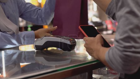 Photo for An upwardly mobile Asian Muslim man using a mobile phone - smartwatch to pay for a product at a sale terminal with nfc identification payment for verification and authentication - Royalty Free Image