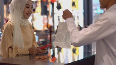 Photo for An upwardly mobile Asian Muslim man - woman using a mobile phone to scan the QR Code to pay at sale terminal with identification payment for verification and authentication - Royalty Free Image