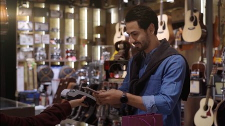 Foto de Un hombre de Oriente Medio ascendente y móvil que usa un teléfono móvil: smartwatch para comprar productos en el terminal del punto de venta en una tienda minorista con pago de identificación nfc para verificación - Imagen libre de derechos