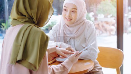 Photo for Young beautiful Asian Muslim women enjoying a relaxing moment working and playing with mobile phone in the coffee shop on a bright sunny day - Royalty Free Image
