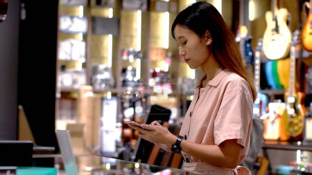 Foto de Mujer asiática joven que usa el teléfono móvil para comprar productos en el terminal del punto de venta en una tienda minorista con tecnología de pago de identificación de radiofrecuencia nfc de comunicación de campo cercano - Imagen libre de derechos