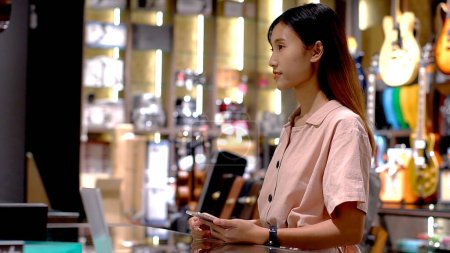 Foto de Mujer asiática joven que usa el teléfono móvil para comprar productos en el terminal del punto de venta en una tienda minorista con tecnología de pago de identificación de radiofrecuencia nfc de comunicación de campo cercano - Imagen libre de derechos