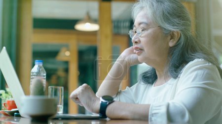 Téléchargez les photos : Femme d'affaires asiatique retraitée active aime travailler sur sa propre petite entreprise en ligne et se détendre dans un coffeeshop par une journée ensoleillée - en image libre de droit