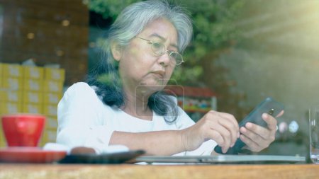Foto de Alta activa jubilada mujer de negocios asiática disfrutar de trabajar en su propia pequeña empresa en línea y relajarse en un coffeeshop en un día soleado brillante - Imagen libre de derechos
