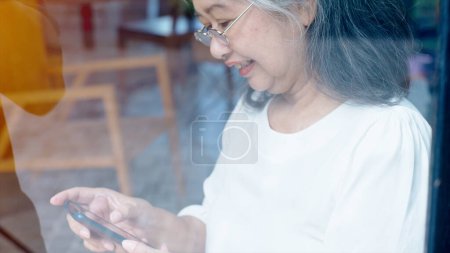 Photo for Active senior retired Asian business woman enjoy working on her own online small business and relaxing in a coffeeshop on a bright sunny day - Royalty Free Image
