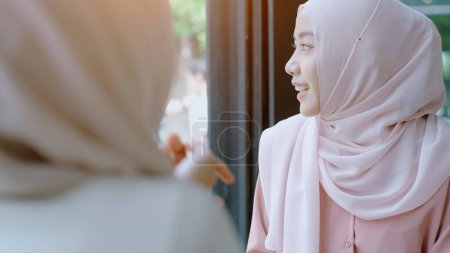 Téléchargez les photos : Jeunes belles femmes musulmanes asiatiques profitant d'un moment de détente en travaillant et en jouant avec un téléphone portable dans le café par une journée ensoleillée - en image libre de droit