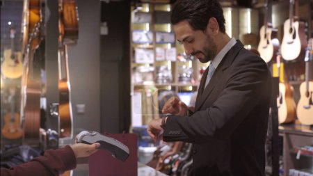 Foto de Un hombre de Oriente Medio ascendente y móvil que usa un teléfono móvil: smartwatch para comprar productos en el terminal del punto de venta en una tienda minorista con pago de identificación nfc para verificación - Imagen libre de derechos