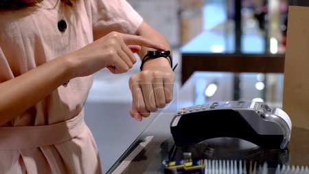 Photo for Young Asian woman using mobile phone - smartwatch to purchase product at the point of sale terminal in a retail store with near field communication nfc radio frequency identification payment - Royalty Free Image