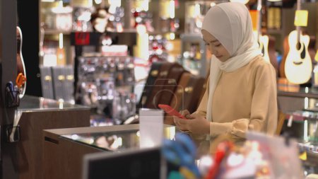 Téléchargez les photos : Un musulman asiatique à la hausse - une femme utilisant un téléphone portable pour scanner le code QR afin de payer au terminal de vente avec paiement d'identification pour vérification et authentification - en image libre de droit