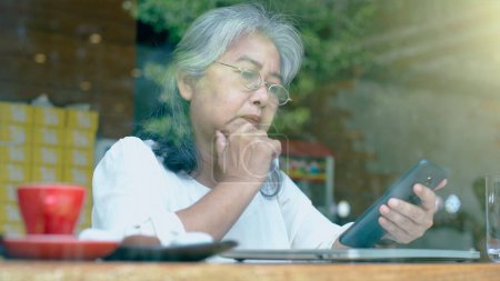Photo for Active senior retired Asian business woman enjoy working on her own online small business and relaxing in a coffeeshop on a bright sunny day - Royalty Free Image